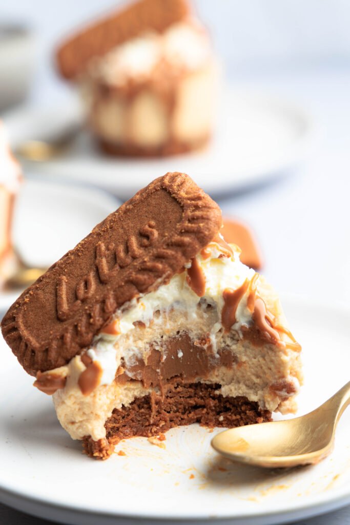 Angebissener Mini-Lotus-Käsekuchen mit cremigen Schichten und einem reichhaltigen Lotus Biscoff Kern, garniert mit Schlagsahne und einem Lotus-Keks.