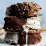 Geschmolzenes Eis tropft von gestapelten Eis-Sandwiches mit Schokoladenglasur und knusprigen Nüssen.