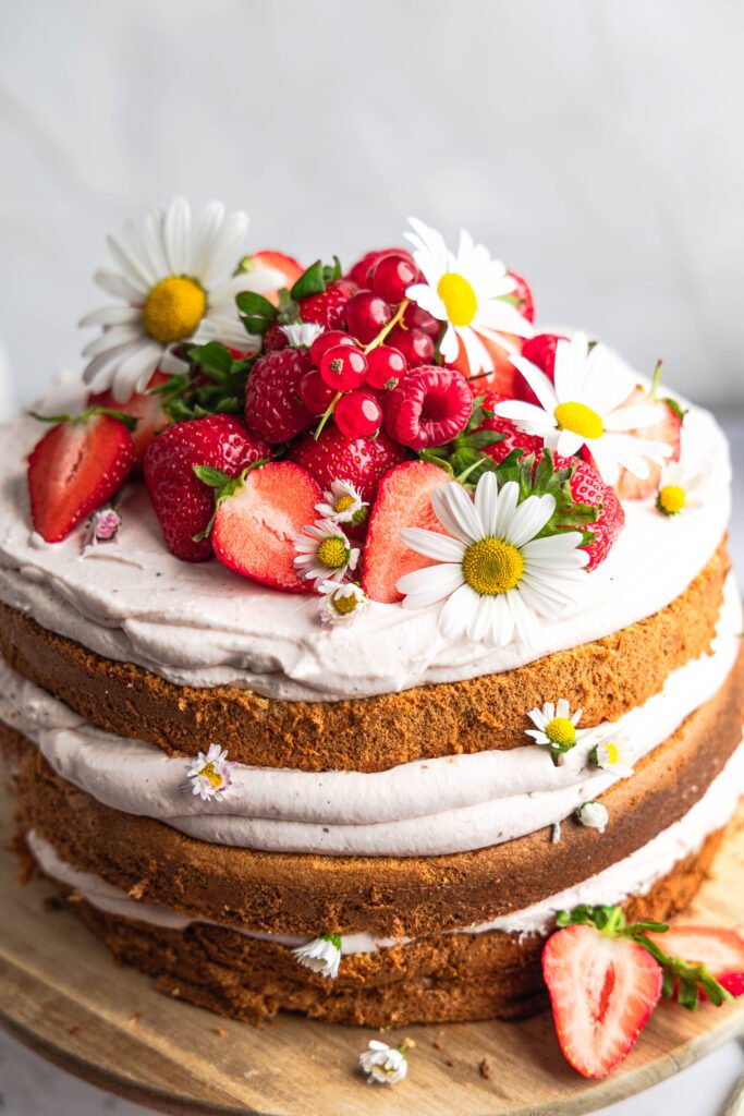 Gestapelter Naked Cake mit Chai-Latte-Biskuit, Erdbeer-Mascarpone-Creme, frischen Erdbeeren und Himbeeren, verziert mit essbaren Gänseblümchen.