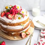 Layered naked cake with chai latte sponge, strawberry mascarpone cream, fresh strawberries and raspberries, decorated with edible daisies.