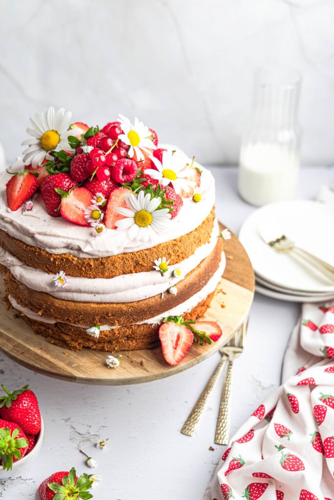 Layered naked cake with chai latte sponge, strawberry mascarpone cream, fresh strawberries and raspberries, decorated with edible daisies.