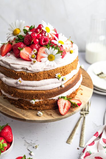 Vrstvená nahá torta s korpusom z chai latte cesta, jahodovým mascarpone krémom, čerstvými jahodami a malinami, ozdobená margarétkami.