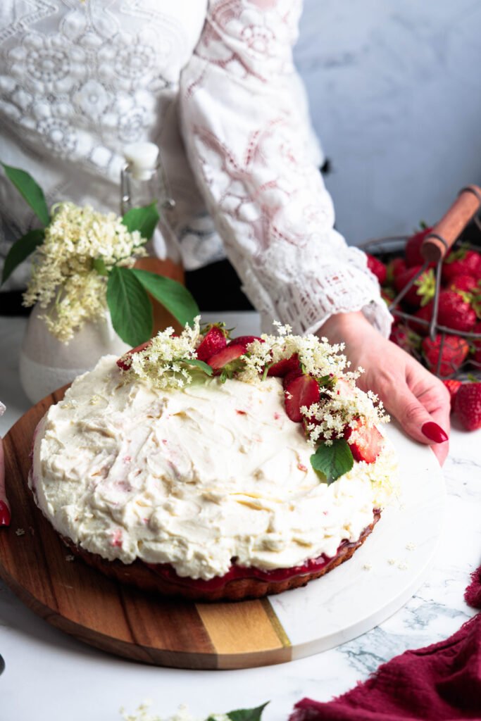 Jahodovo-bazový tart s nadýchaným mascarpone krémom, ozdobený čerstvými jahodami a kvetmi bazy na drevenom podnose.