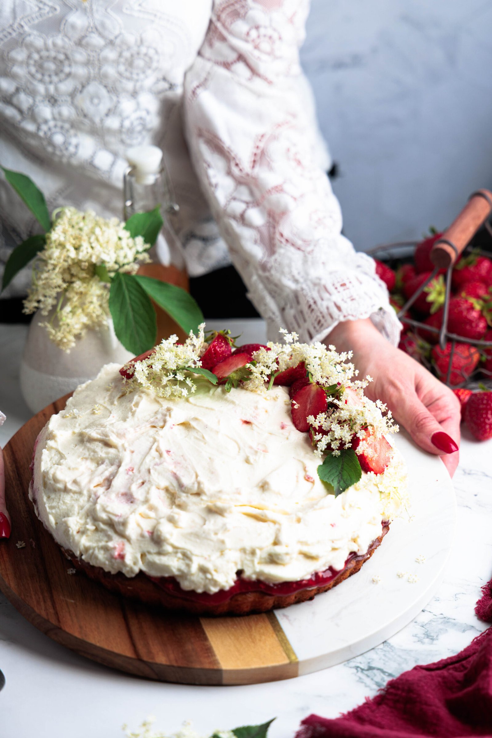 Jahodovo-bazový tart s nadýchaným mascarpone krémom, ozdobený čerstvými jahodami a kvetmi bazy na drevenom podnose.