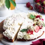 Elderflower strawberry tart with whipped mascarpone cream, decorated with fresh strawberries and elderflowers on a wooden cake board.