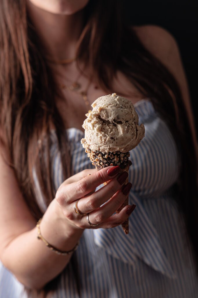 Woman in a striped dress holding hazelnut ice cream with white Kinder Bueno in a cone.